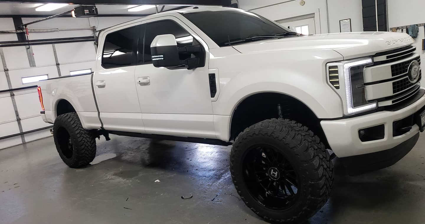 White lifted Ford Super Duty pickup with freshly tinted windows inside the D&R shop